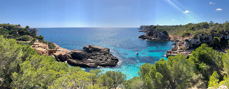 a daytime shot of a cove with clear water, there's one boat out and a few houses along the shoreline